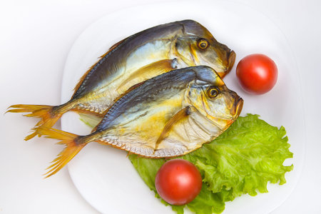 Smoked fish on white plate with vegetables on isolated background. Fresh green salad and red...