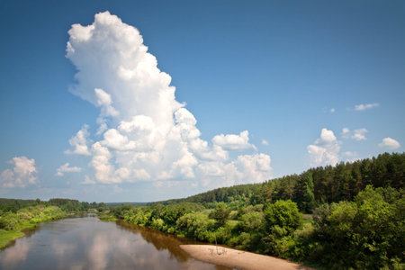 Beautiful rural landscape with big cloud on blue sky. Big river and green lush trees along the...
