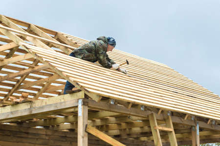 Construction of a wooden house in a rural area. The construction of the roof. Adult men engaged in construction. Tools in their hands. Cloudy cool day.の写真素材