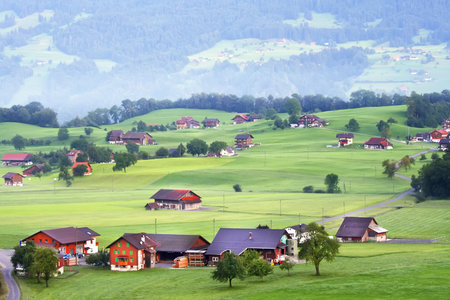 Beautiful houses in the Swiss mountain valley at dawn. Rural place.  Big beautiful mountains. Morning fog in the mountains. Green grass and trees.の写真素材