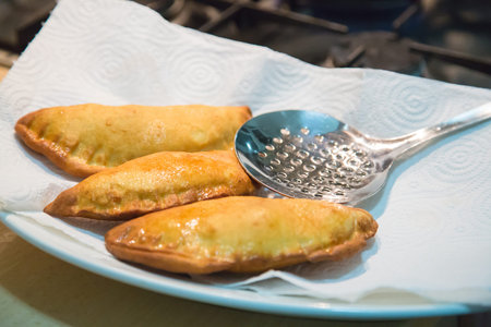 Ready-made ruddy fried panzerotti on a white plate on a napkin. The cooking spoon skimmer is on the plateの写真素材