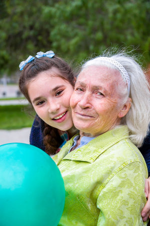 Cute teenage girl is hugging her beautiful smiling granny in cheek.