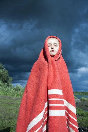The girl wrapped in a red blanket on the background of a stormy skyの写真素材