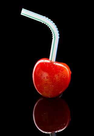 Cherry with straw isolated on black - fresh juice drink conceptの写真素材
