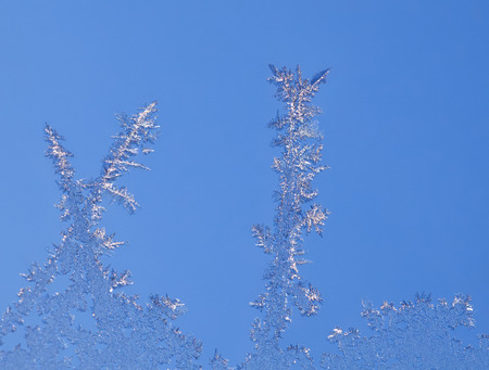 Macro of hoarfrost ornament on window glass over blue sky backgroundの写真素材