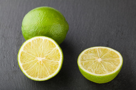 Closeup of whole and sliced on half green limes over black slate plate
の写真素材