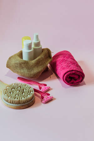 White bottles of body care products, a wooden massage counter, a pink towel, pink razors stand against a pink background.の写真素材
