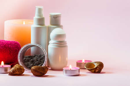 Basic hygiene products in white bottles, an alginate mask and a pink towel stand against a pink background next to burning candles.の写真素材