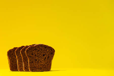 FOUR slices of sourdough black bread stand side by side against a bright yellow background.の写真素材