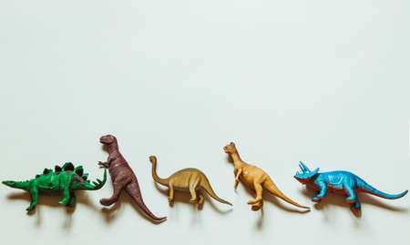Five toy dinosaurs stand in a row against a white background with plenty of space to insert.の写真素材
