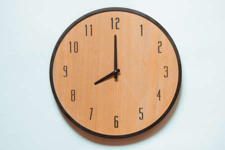 Wooden mechanical wall clock with black numerals and black hands showing seven o'clock.の写真素材