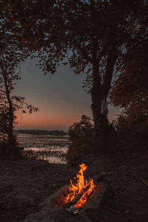 Bright orange glowing bonfire near a quiet river during evening sunset.の写真素材