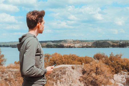 A young guy in a sweatshirt holds a phone in his hands and enjoys the view of the quarry and the...