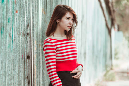 Pretty girl in a striped long-sleeved T-shirt near an aluminum fence and looks to the side.の写真素材