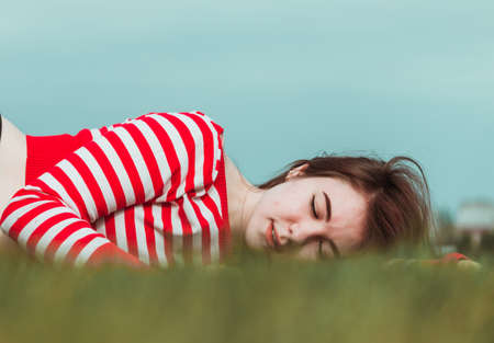 A girl with dark hair and a striped T-shirt lies on the grass and enjoys the warmth of spring.の写真素材