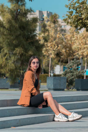 Stylish girl in sunglasses sits outdoors in the park and smiles at the camera.の写真素材
