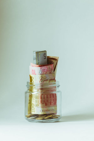 A small glass jar with money stands on a white background.