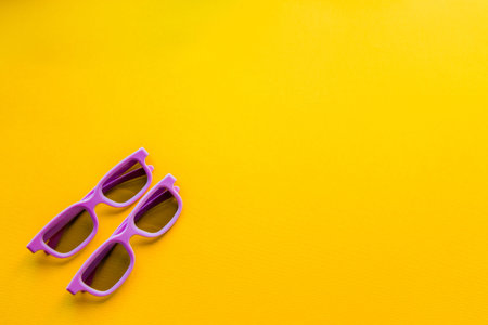A pair of purple 3d glasses for watching a movie in a cinema lie on a bright yellow background.