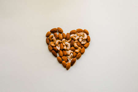Cashews and almonds are laid out on a white background in the shape of a heart. Proper nutrition, healthy snack. Healthy heart.の写真素材