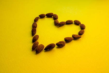Almonds are laid out on a yellow background in the shape of a heart. Proper nutrition, healthy snack. Healthy heart.の写真素材