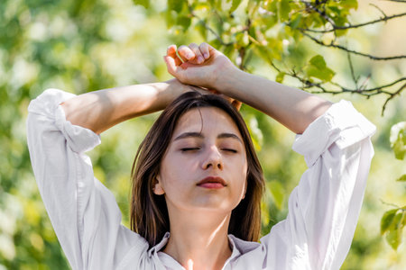 A young beautiful girl with dark hair and in a white shirt closed her eyes and breathes fresh air in...