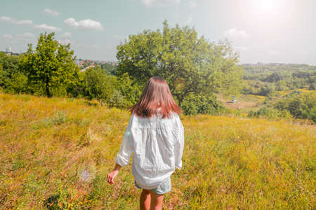 A girl with smooth dark hair in a white shirt runs along the lawn on a warm sunny day. High quality photoの写真素材