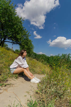 A girl in a white shirt, denim shorts and white sneakers lies on the lawn with her eyes closed in warm weather. High quality photoの写真素材