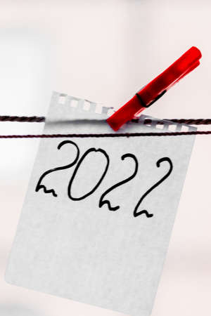 The number 2022 is written in black marker on a scrap of notepad and hangs with a red clothespin. New year 2022. High quality photoの写真素材