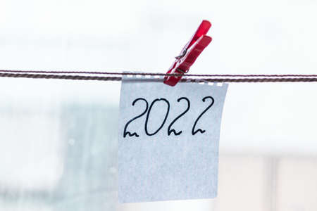 The number 2022 is written in black marker on a scrap of notepad and hangs with a red clothespin. New year 2022. High quality photoの写真素材