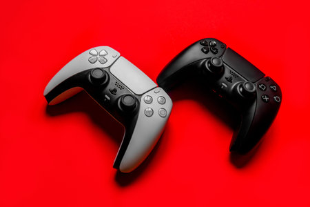 Ukraine - December 10, 2021. White and black wireless PlayStation 5 Dualsense gamepads on a red...