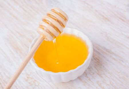 Honey with a stick in a white bowl on wooden tableの写真素材