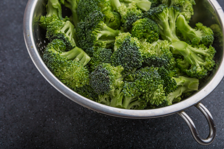 pieces of broccoli in a sieve on a black table. studio shotの写真素材