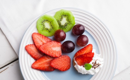 Fresh fruit: kiwi, strawberries, grapes on a blue plate. studio shotの写真素材