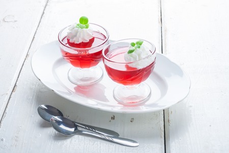 red jelly with whipped cream in a glass bowl on white table. studio shotの写真素材