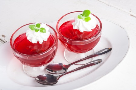 red jelly with whipped cream in a glass bowl on white table. studio shotの写真素材