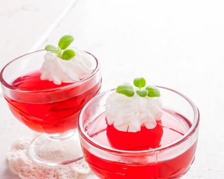 red jelly with whipped cream in a glass bowl on white table. studio shotの写真素材