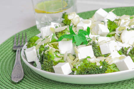 broccoli salad with feta cheese and almonds on a white plateの写真素材