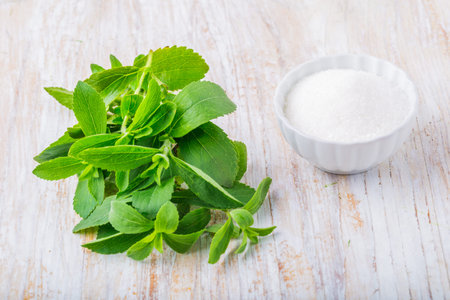 fresh stevia leaves and small bowl with sugar on a white wooden table. studio shot