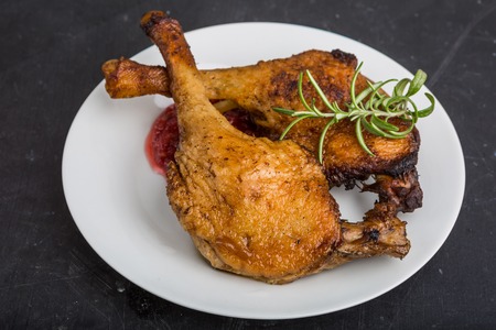 Roast duck legs with cranberries and fresh rosemary on white plateの写真素材