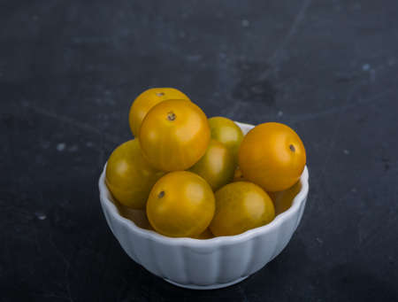 Yellow cherry tomatoes in white bowl on black tableの写真素材