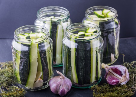 Marinated zucchini pieces in jars on black wooden tableの写真素材