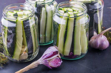 Marinated zucchini pieces in jars on black wooden tableの写真素材