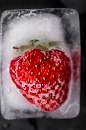 Ice cube with strawberry on black wooden tableの写真素材