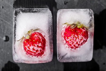 Ice cubes with strawberries on black wooden tableの写真素材