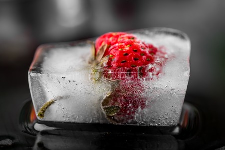 Ice cube with strawberry on black wooden tableの写真素材