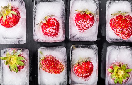 Ice cubes with strawberries on black wooden tableの写真素材