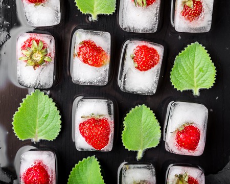 Ice cubes with strawberries and fresh mint leaves on black tableの写真素材