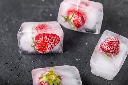 Ice cubes with strawberries on black wooden tableの写真素材
