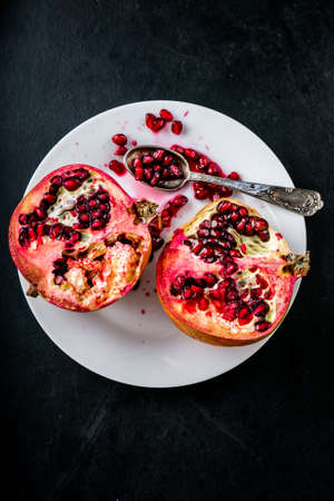 Fresh juicy pomegranates on white plate on black wooden tableの写真素材