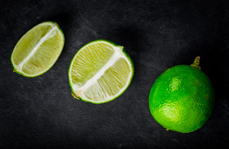 Fresh limes with slices on black wooden background